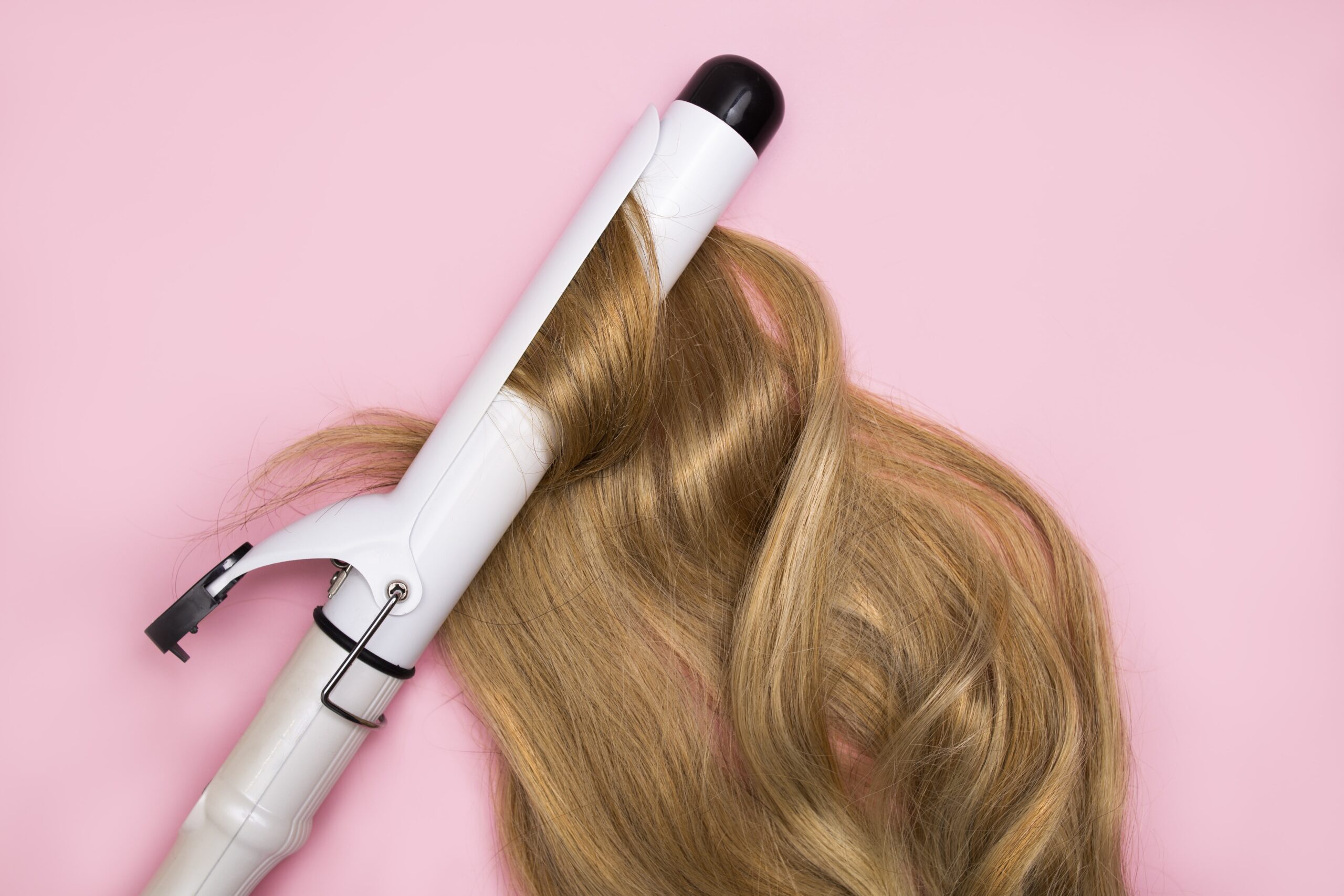curling-blonde-hair-large-diameter-curling-iron-pink-background-min