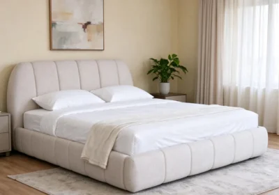 Lit matelassé 140x190 cm en tissu beige à surpiqûres verticales, dans une chambre lumineuse