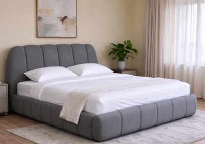 Lit matelassé 160x200 cm en tissu gris à surpiqûres verticales, dans une chambre lumineuse