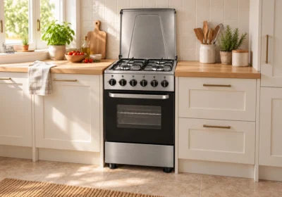 Cuisinière gaz 50x50 cm grise 4 feux avec couvercle métal ouvert, installée dans une cuisine lumineuse